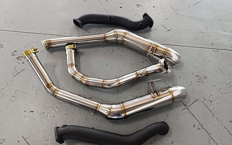 Complete custom stainless exhaust system laid beside the original exhaust